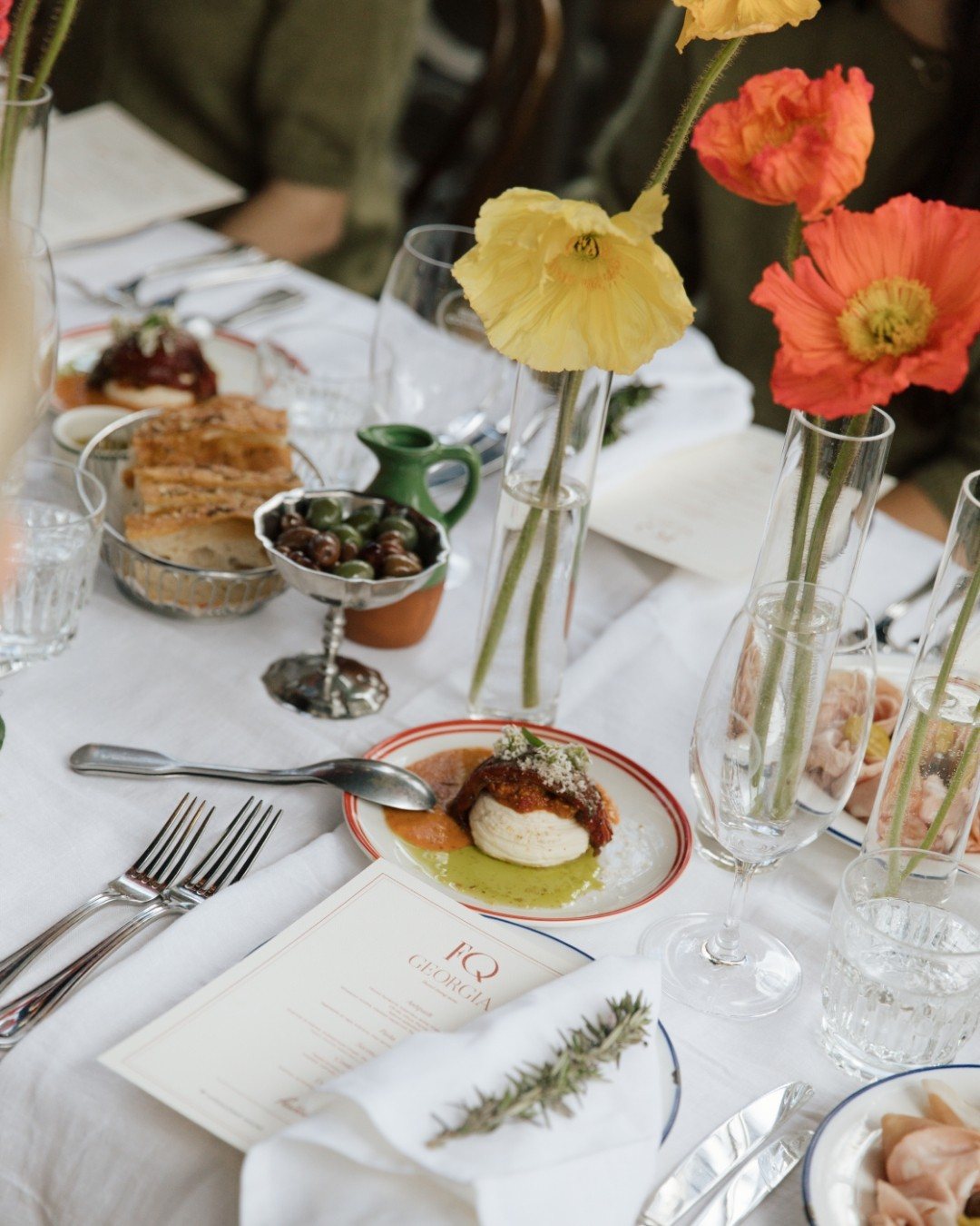 A table set with poppies, burrata, focaccia and olives, with the printed menu beside the plate
