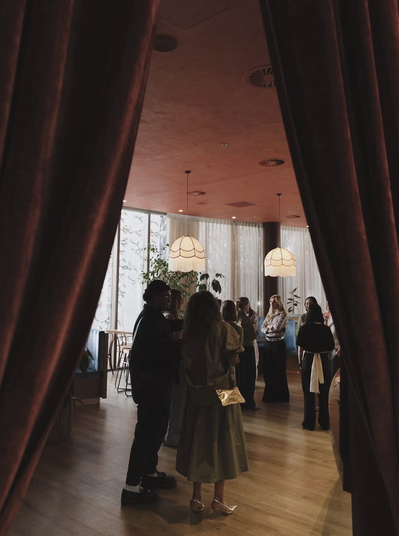Guests gathered under fringed pendant lamps, seen between two velvet curtains