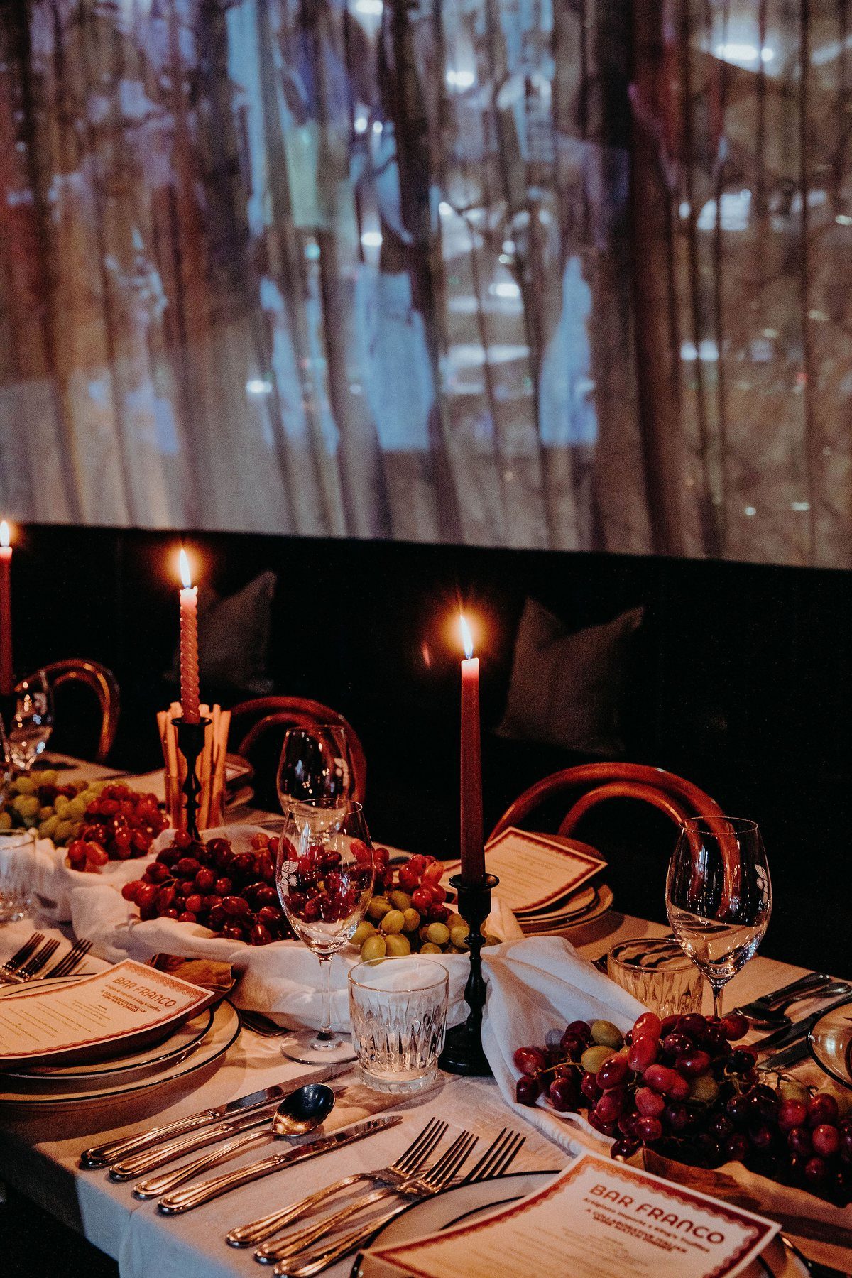 A curtained table set with candles, grapes and printed Bar Franco menus