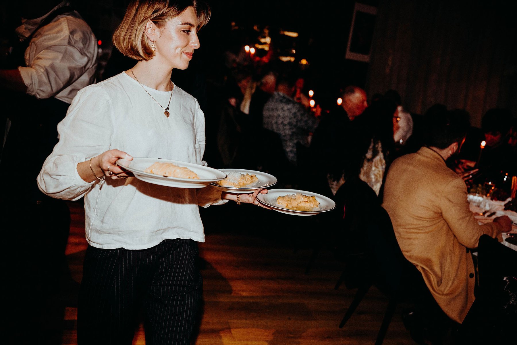 A server carrying plates of fresh pasta to a candlelit table