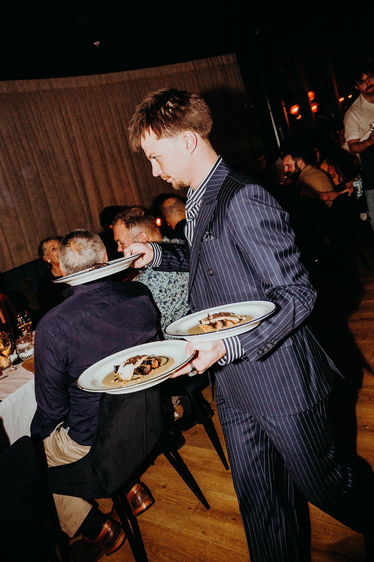 A server in a pinstripe suit carrying plates through the dining room
