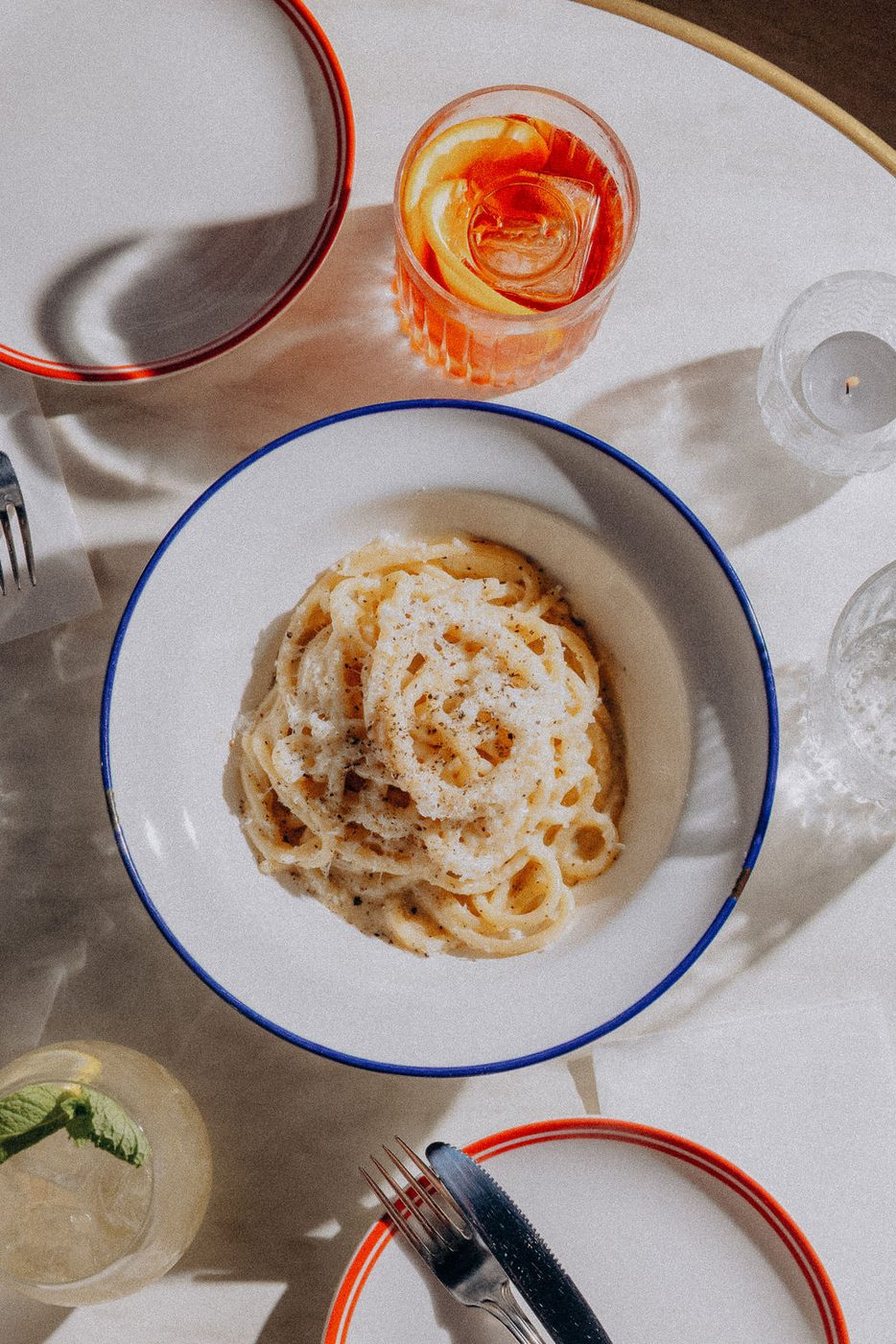 Pici cacio e pepe in a blue-rimmed bowl on the marble, a Negroni beside it in the afternoon sun