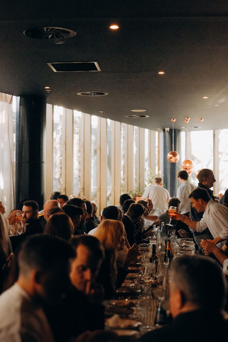 Long tables full of guests upstairs by the wall of windows