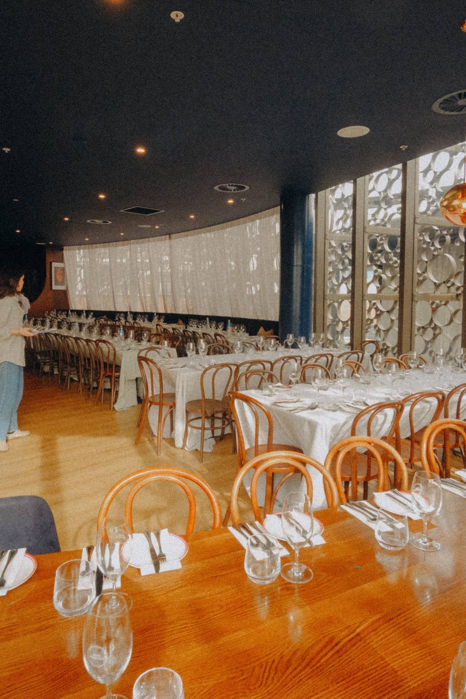 Long tables in white linen set for a dinner upstairs, bentwood chairs and screened windows